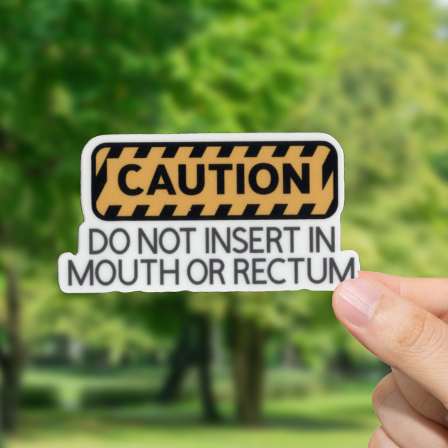Hand holding a 'Caution' sign with 'Do not insert in mouth or rectum' and a blurred green outdoor background
