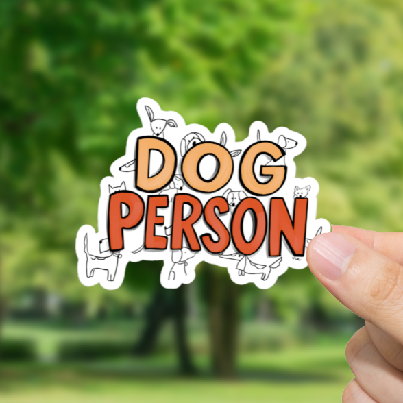 Hand holding a 'Dog Person' sticker with a park background