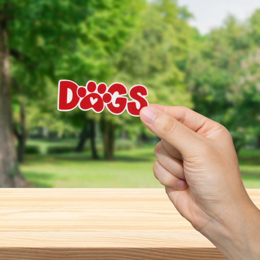 Hand holding a 'DOGS' sign with a blurred park background