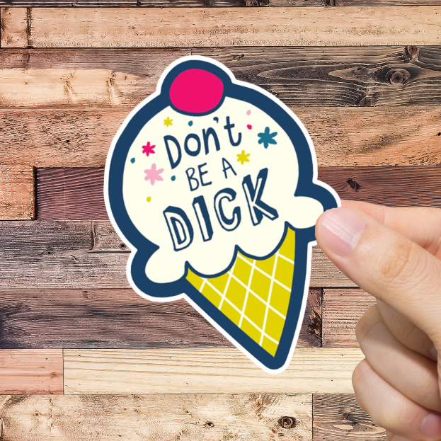 Hand holding a sticker with 'Don't be a dick' text against a wooden background
