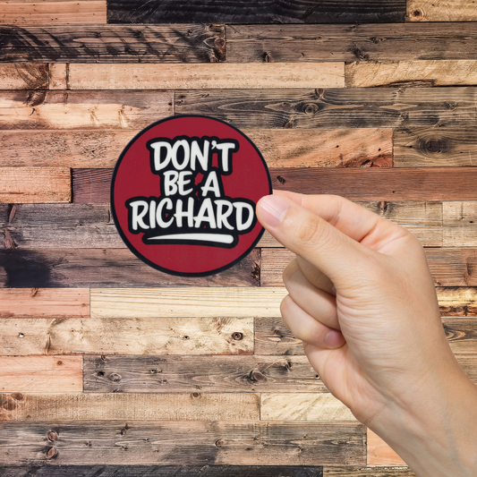 Hand holding a round sticker with 'Don't Be A Richard' text against a wooden background