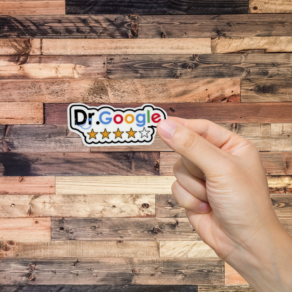 Hand holding a sticker with 'Dr. Google' logo against a wooden background