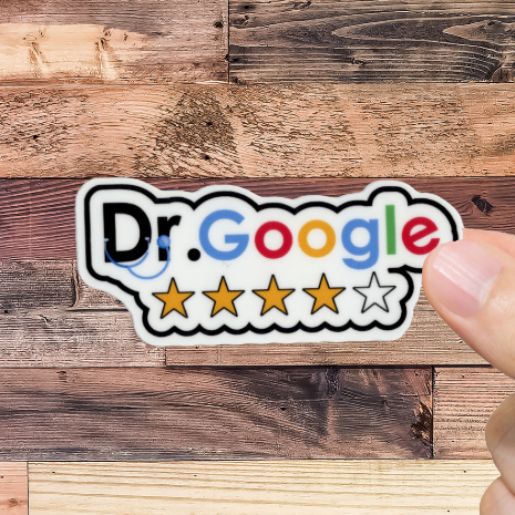Hand holding a sticker with 'Dr. Google' logo against a wooden background