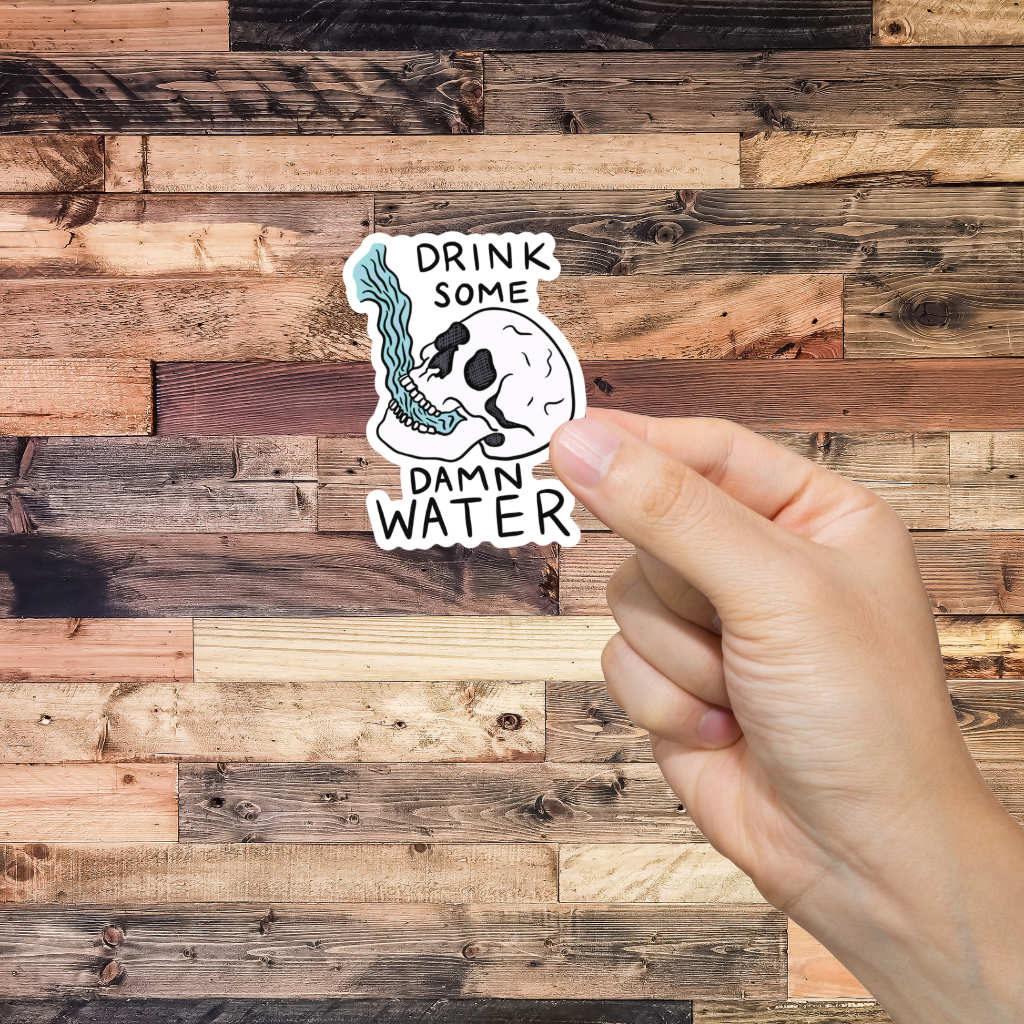 Hand holding a sticker with 'Drink Some Damn Water' text against a wooden background
