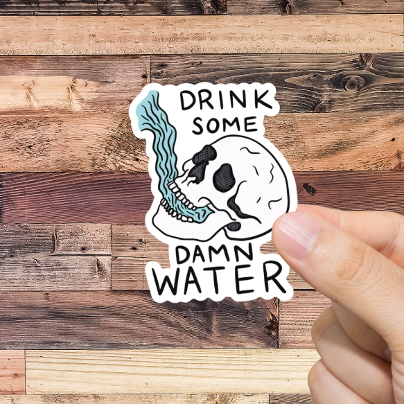 Hand holding a sticker with 'Drink Some Damn Water' text against a wooden background