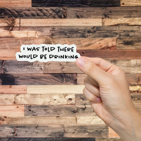 Hand holding a piece of paper with text 'I was told there would be drinking'  against a wooden background