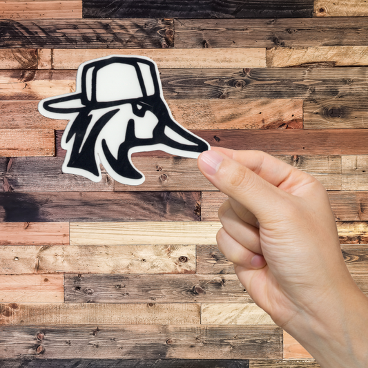 Hand holding a sticker of a duck wearing a cap against a wooden background