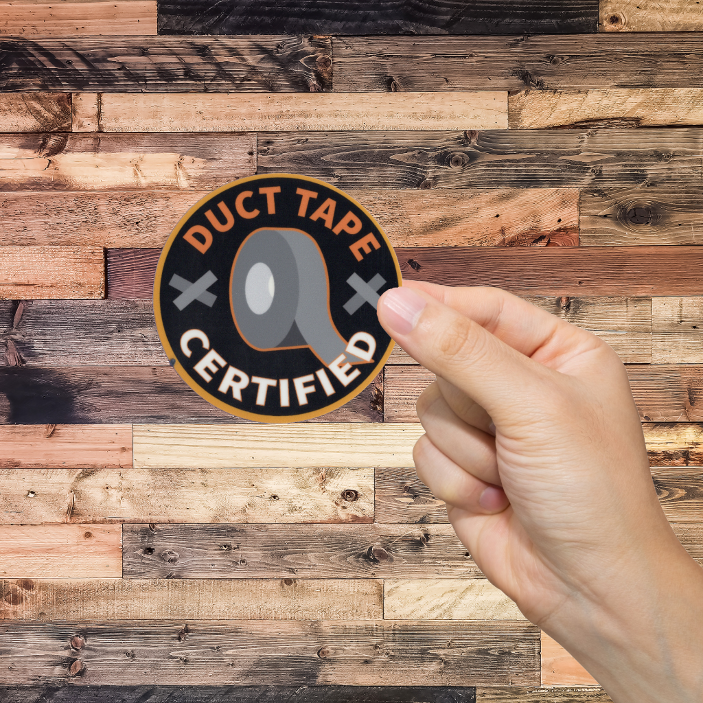 Hand holding a 'Duct Tape Certified' sticker against a wooden background