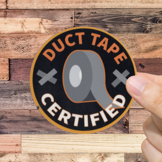 Hand holding a 'Duct Tape Certified' sticker against a wooden background