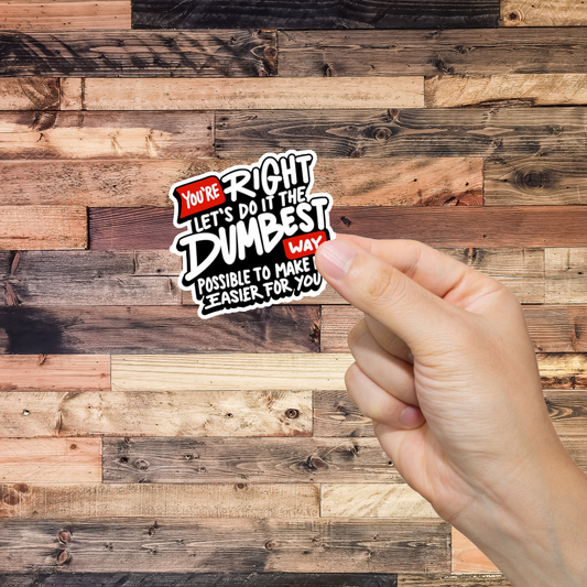 Hand holding a sticker with text 'You're Right Let's do it the Dumbest way possible' against a wooden background