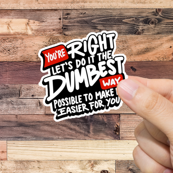 Hand holding a sticker with text 'You're Right Let's do it the Dumbest way possible' against a wooden background