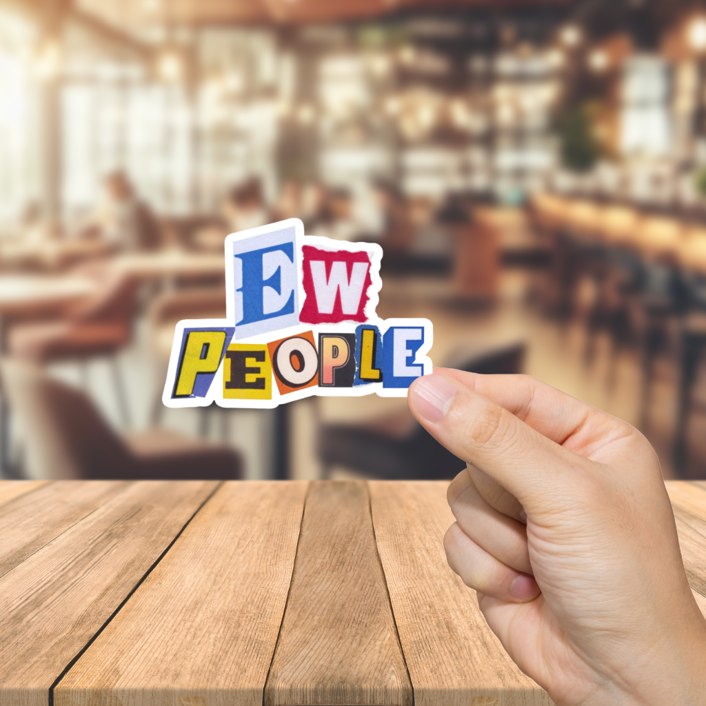 Hand holding a colorful sign with 'EW PEOPLE' text in a blurred restaurant setting