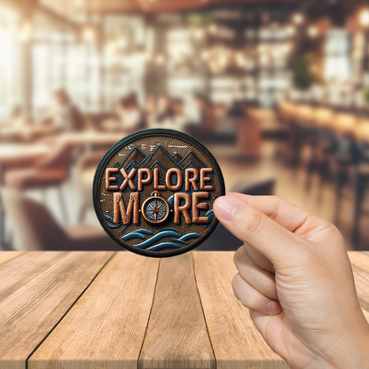 Hand holding a 'Explore More' patch over a blurred bar background