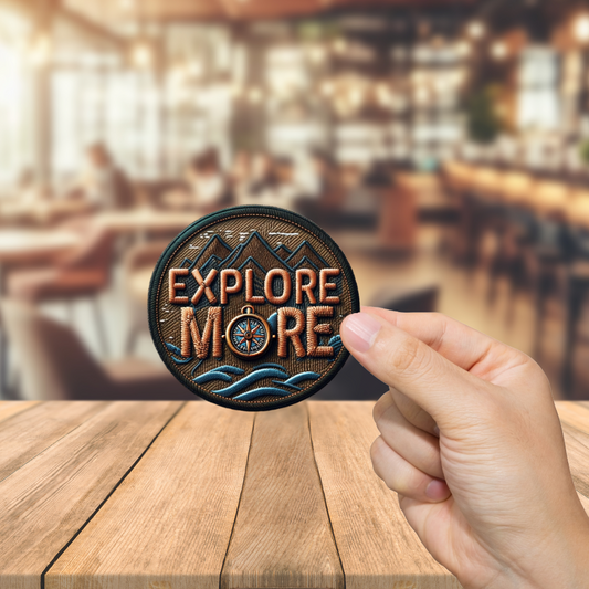 Hand holding a 'Explore More' patch over a blurred bar background