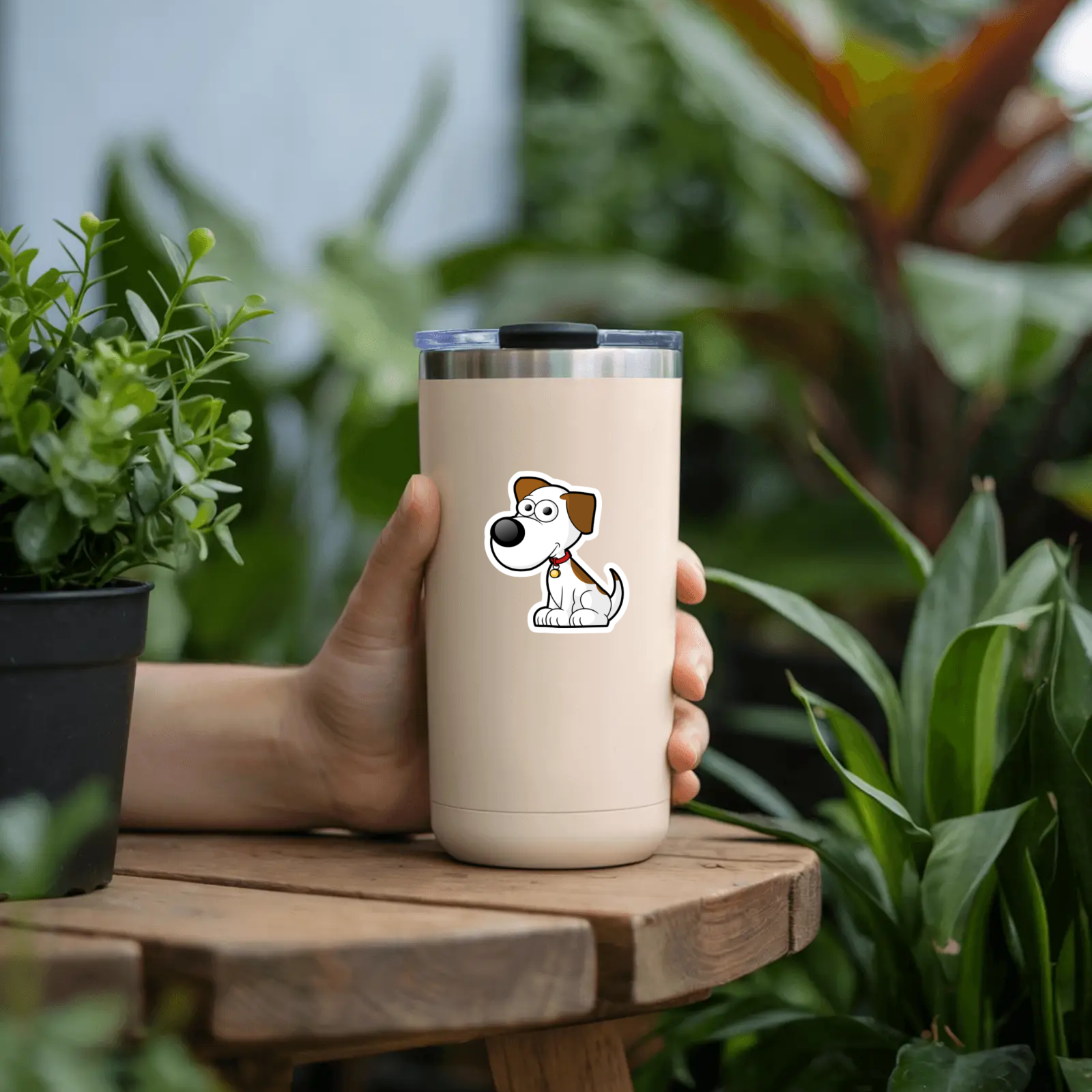 Person holding a beige tumbler with a dog illustration in a garden setting